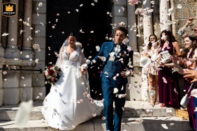 Bride and groom descend church stairs in Renage city, Isère, France, smiling joyfully after their wedding ceremony.